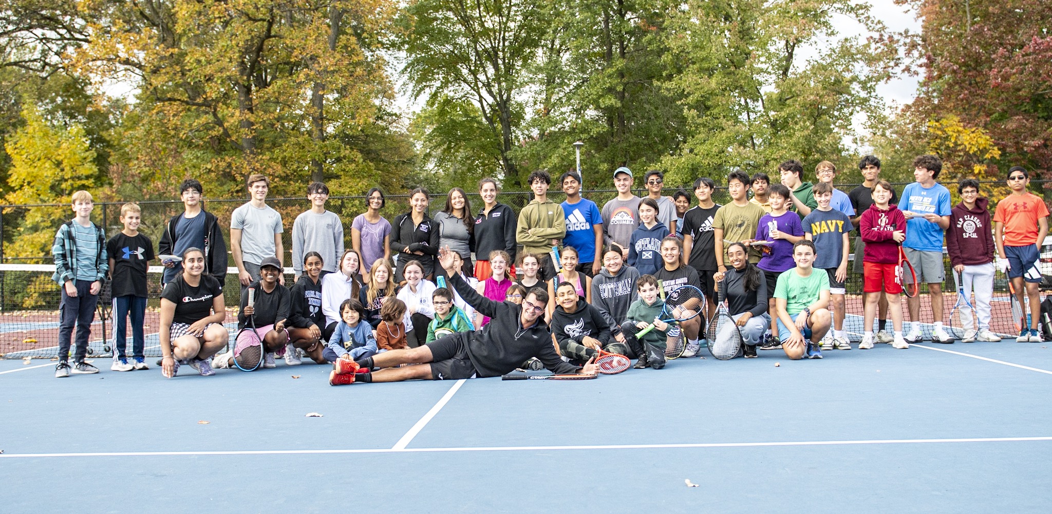 A large group of tennis players and coaches smiling together on court
